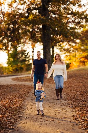 A family walks together on a leaf-covered trail during golden hour sunset in autumn.