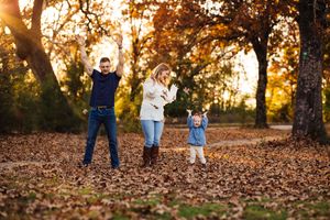A group of people walk through fallen autumn leaves during golden hour in a wooded area.