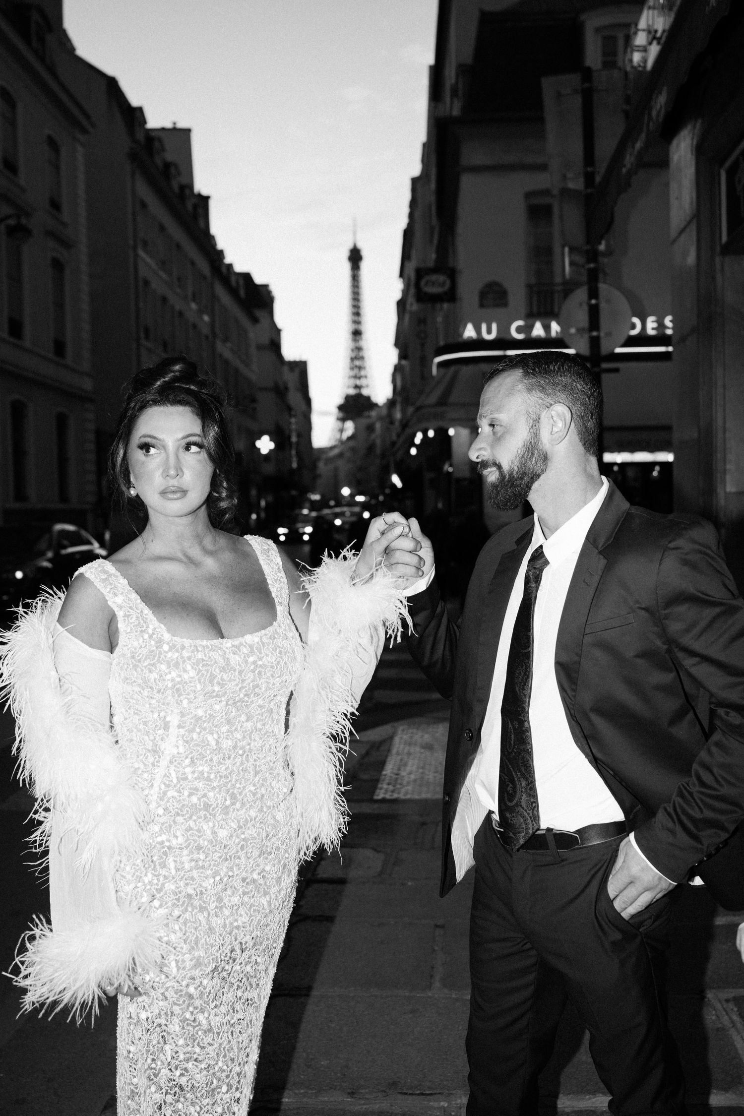 A couple poses on a rooftop terrace in Paris with white balloon arch decorations and the Eiffel Tower visible in background.