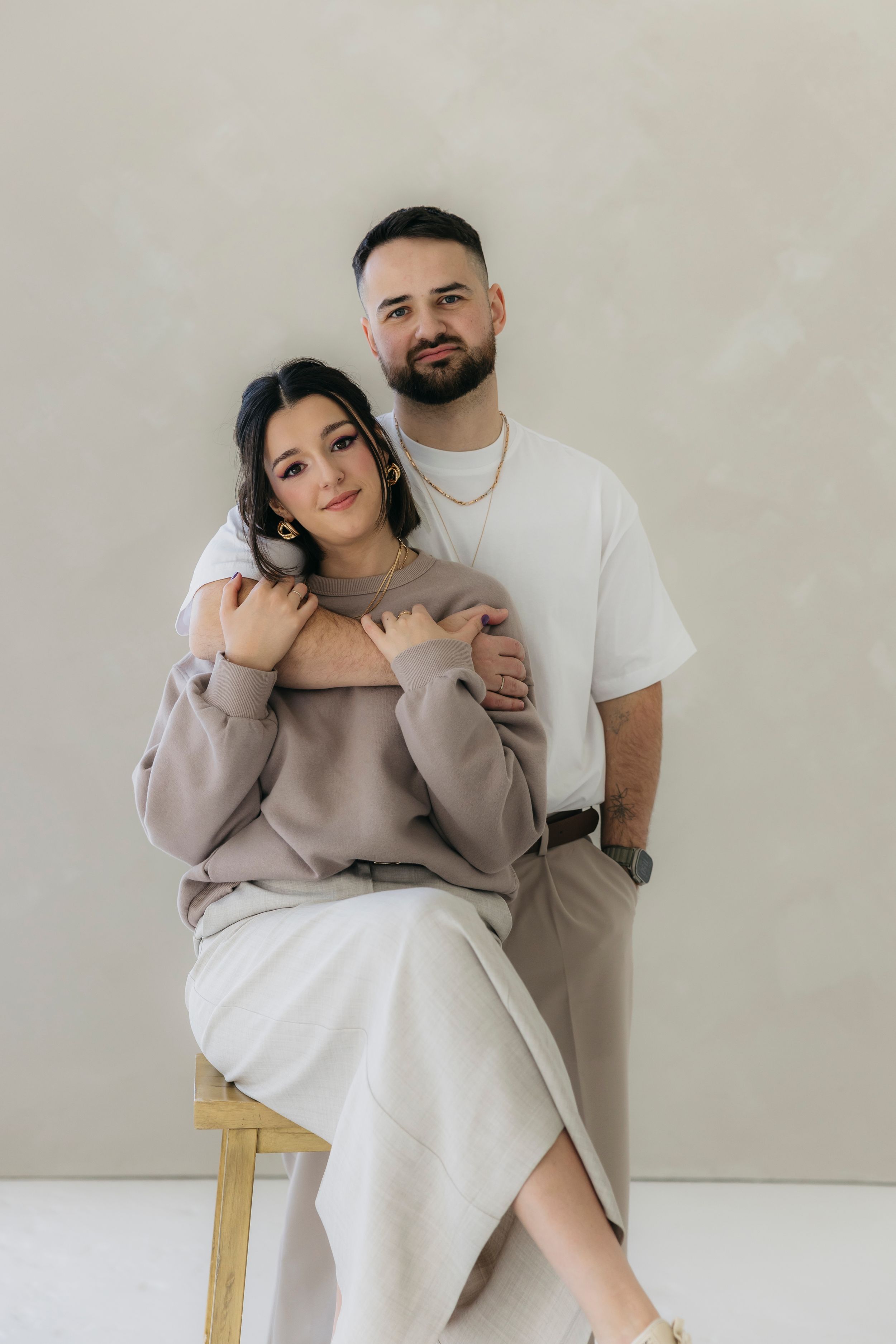A casual studio portrait of a couple in neutral tones against a white background.