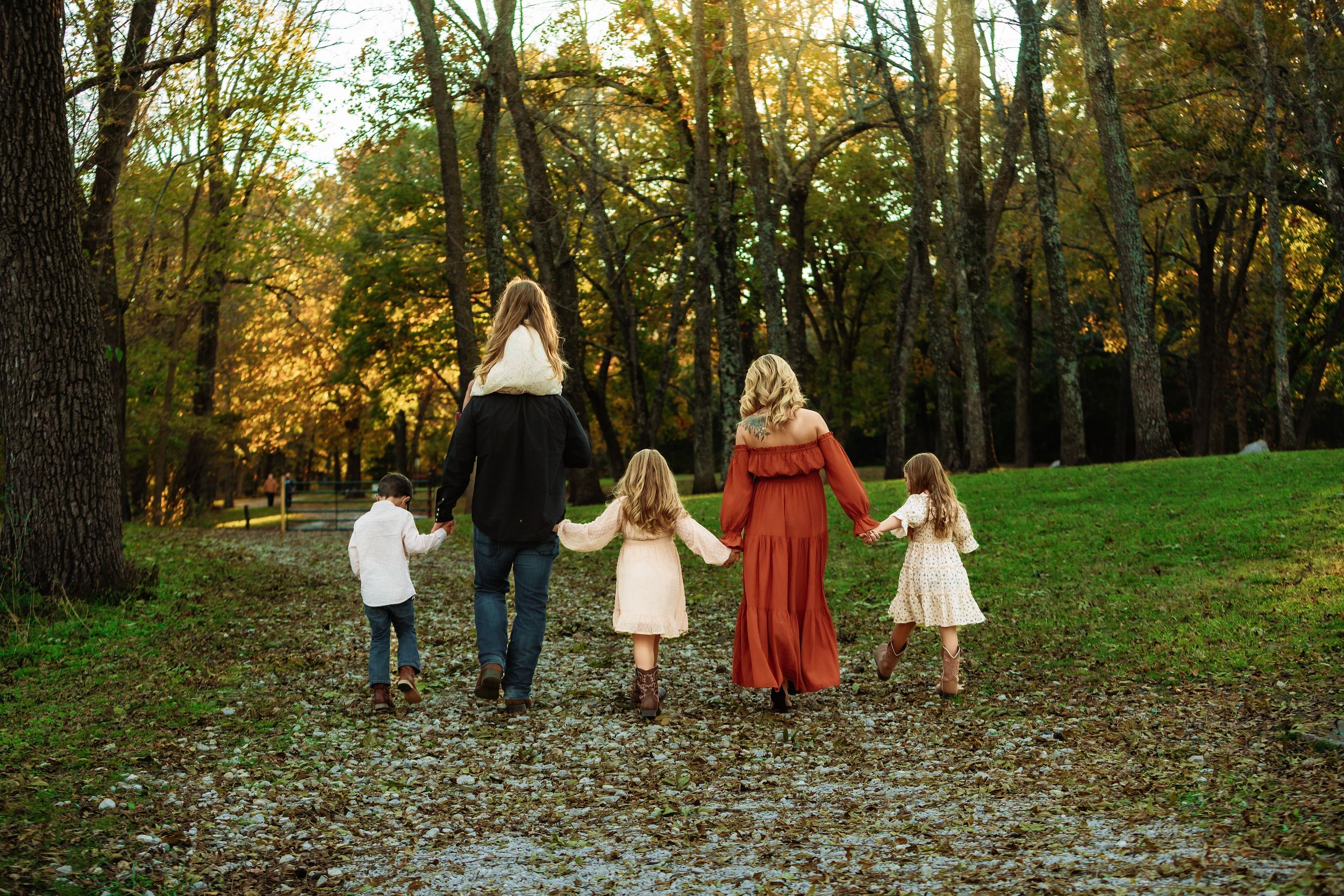 A group walks together through a wooded park during autumn with golden sunlight filtering through the trees.