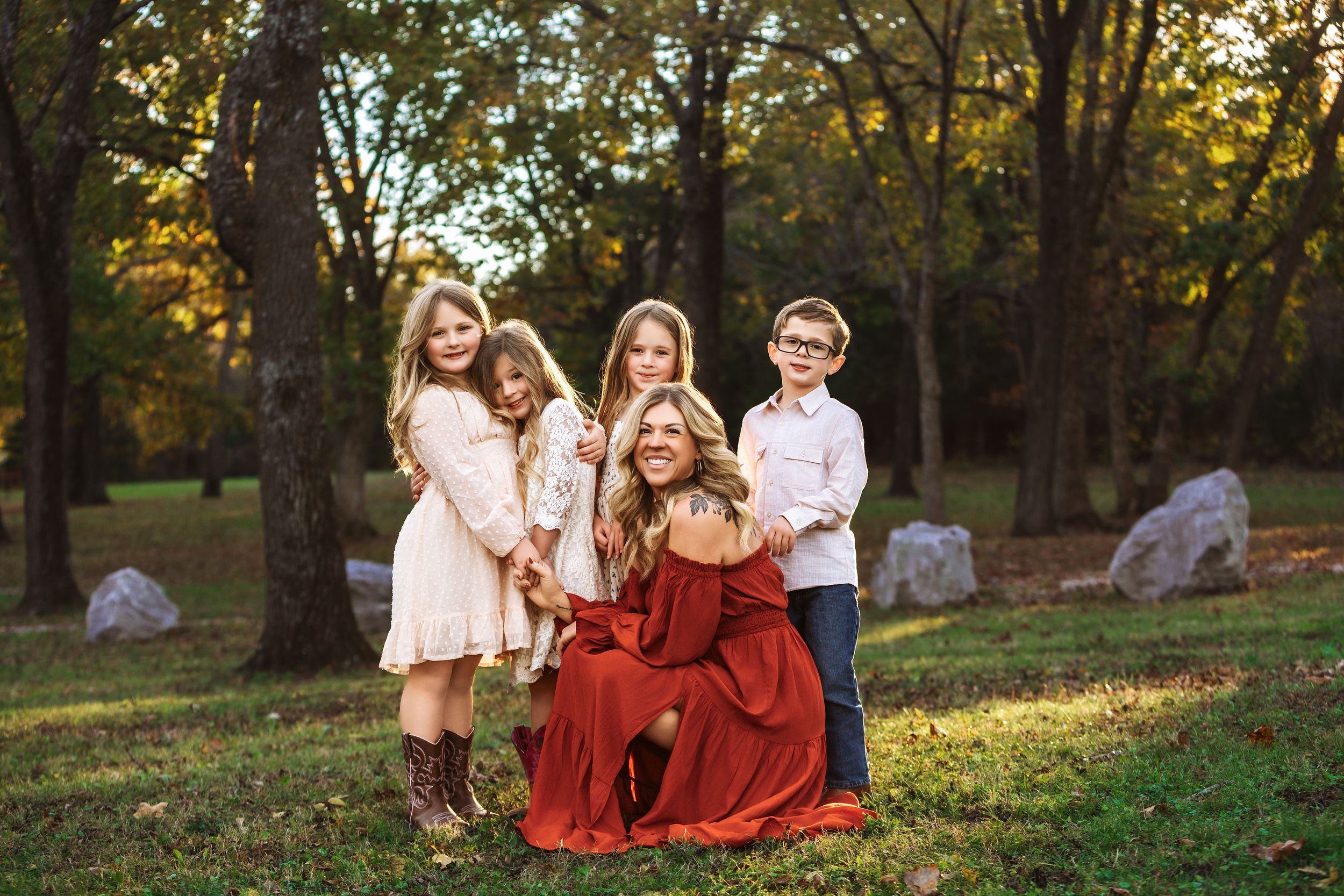 A family wearing red and white outfits sits together on grass during a golden autumn sunset in a park setting.