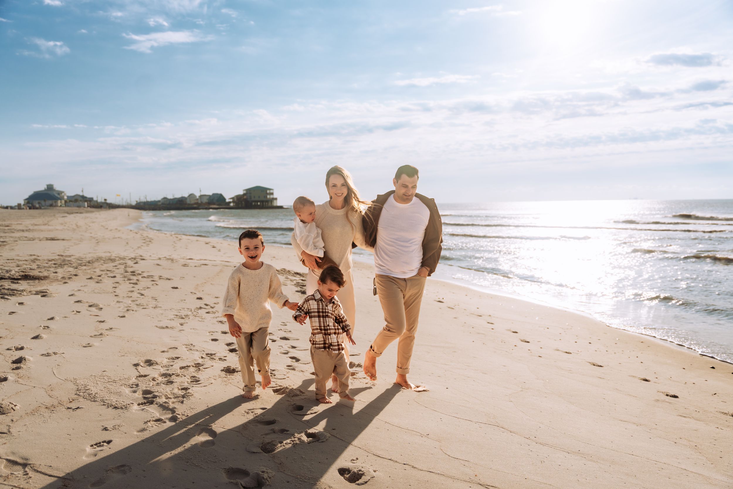 Family walking together on a sandy beach at sunset with waves rolling onto the shore in the background.