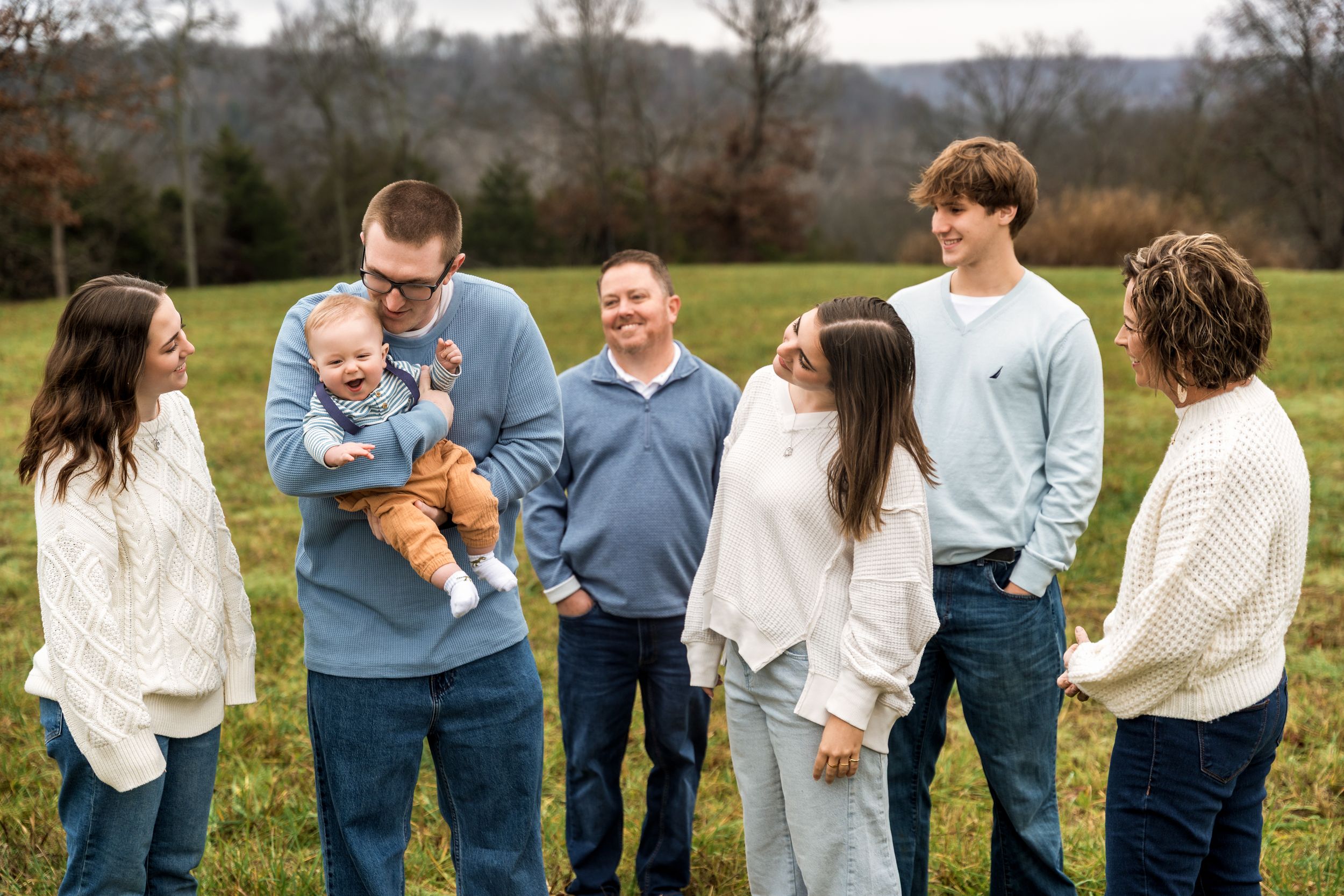 A group gathers outdoors on a grassy hillside for a candid family photo in casual sweaters.
