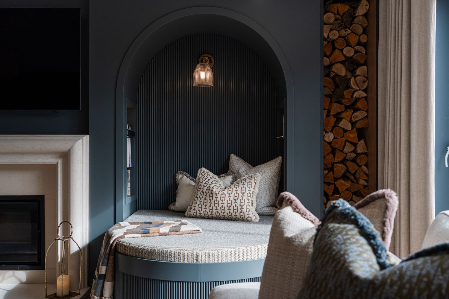 Modern nursery interior with blue walls, stacked firewood, and cozy seating area featuring natural textures and lighting.