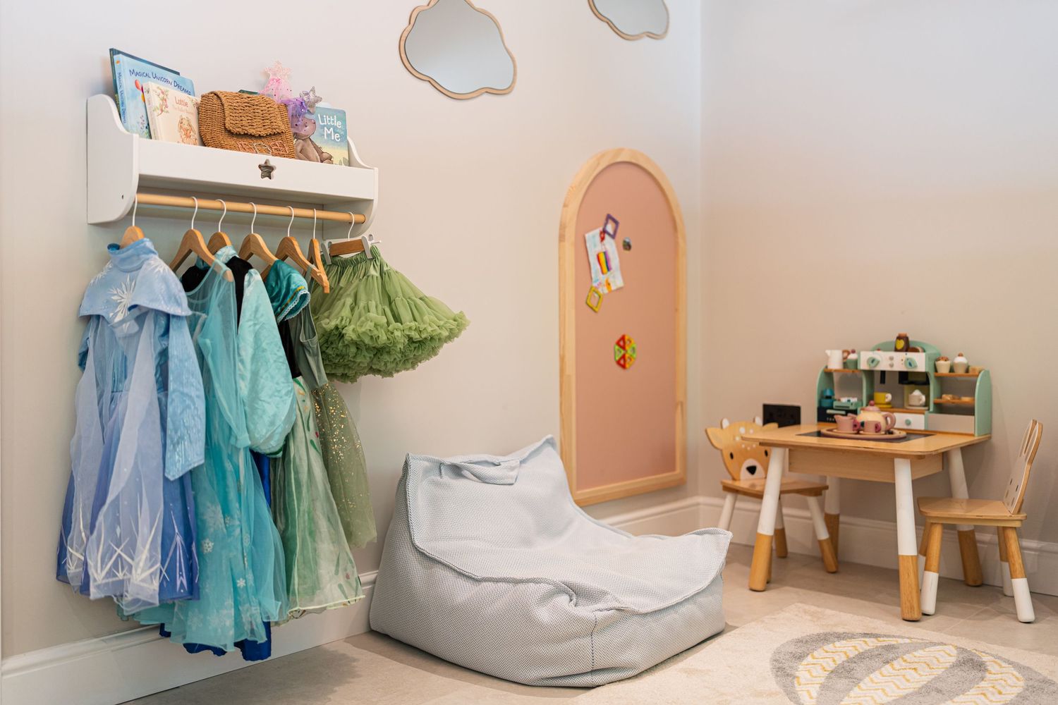 Whimsical children's playroom with pastel walls, cloud decals, and dress-up clothing displayed on wall hooks.