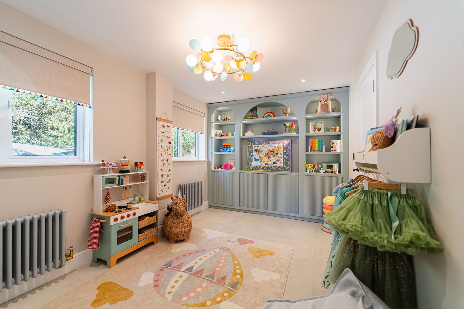 A child's playroom with blue built-in shelving, a toy kitchen set, and a colorful round rug on the floor.