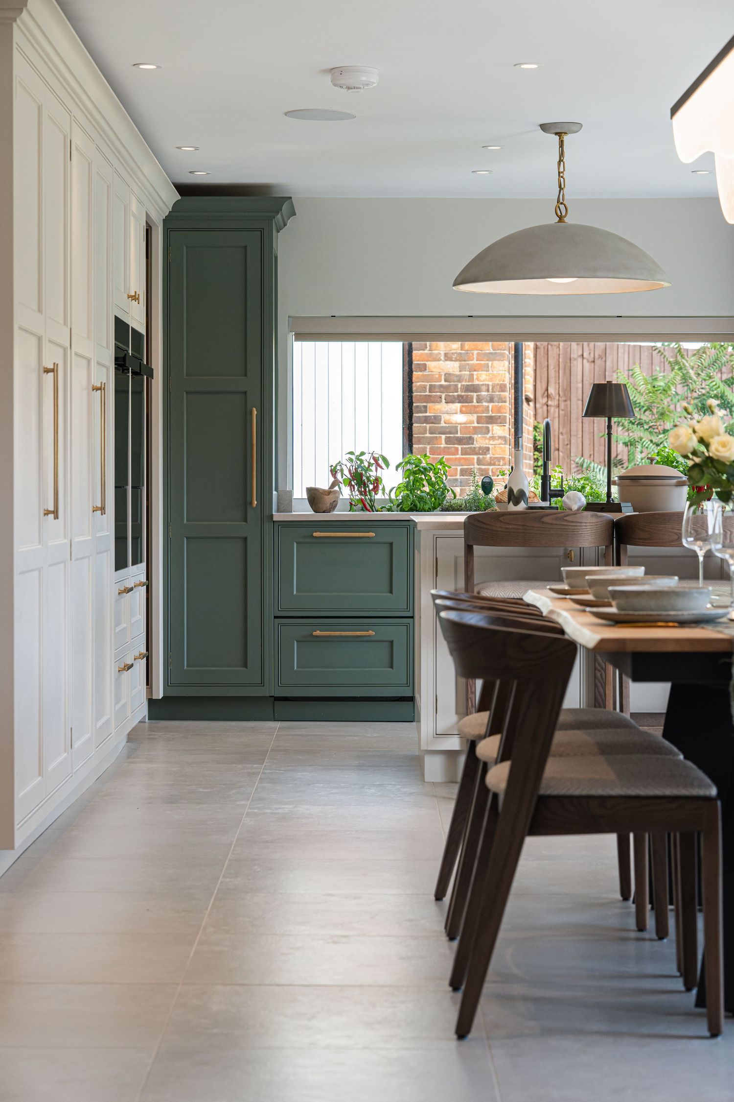Elegant kitchen hallway with green cabinets, wooden dining furniture, and brick accent wall details.