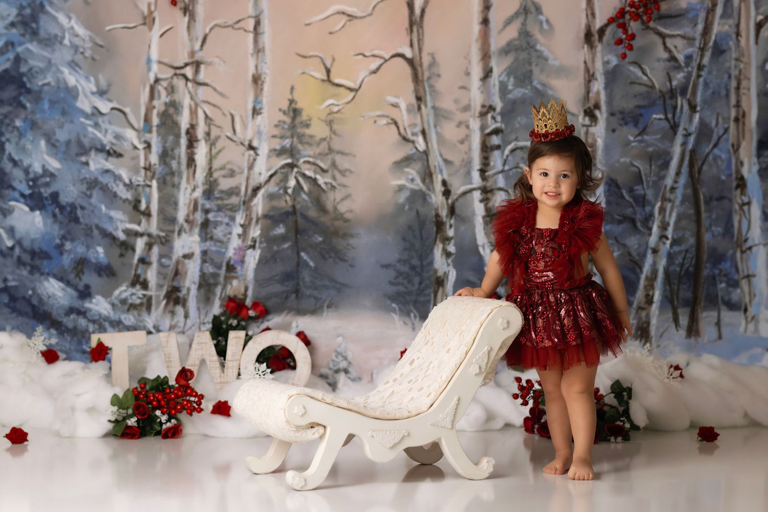 Winter wonderland studio setup with a white sleigh, red roses, birch trees, and snow-covered pine forest backdrop.
