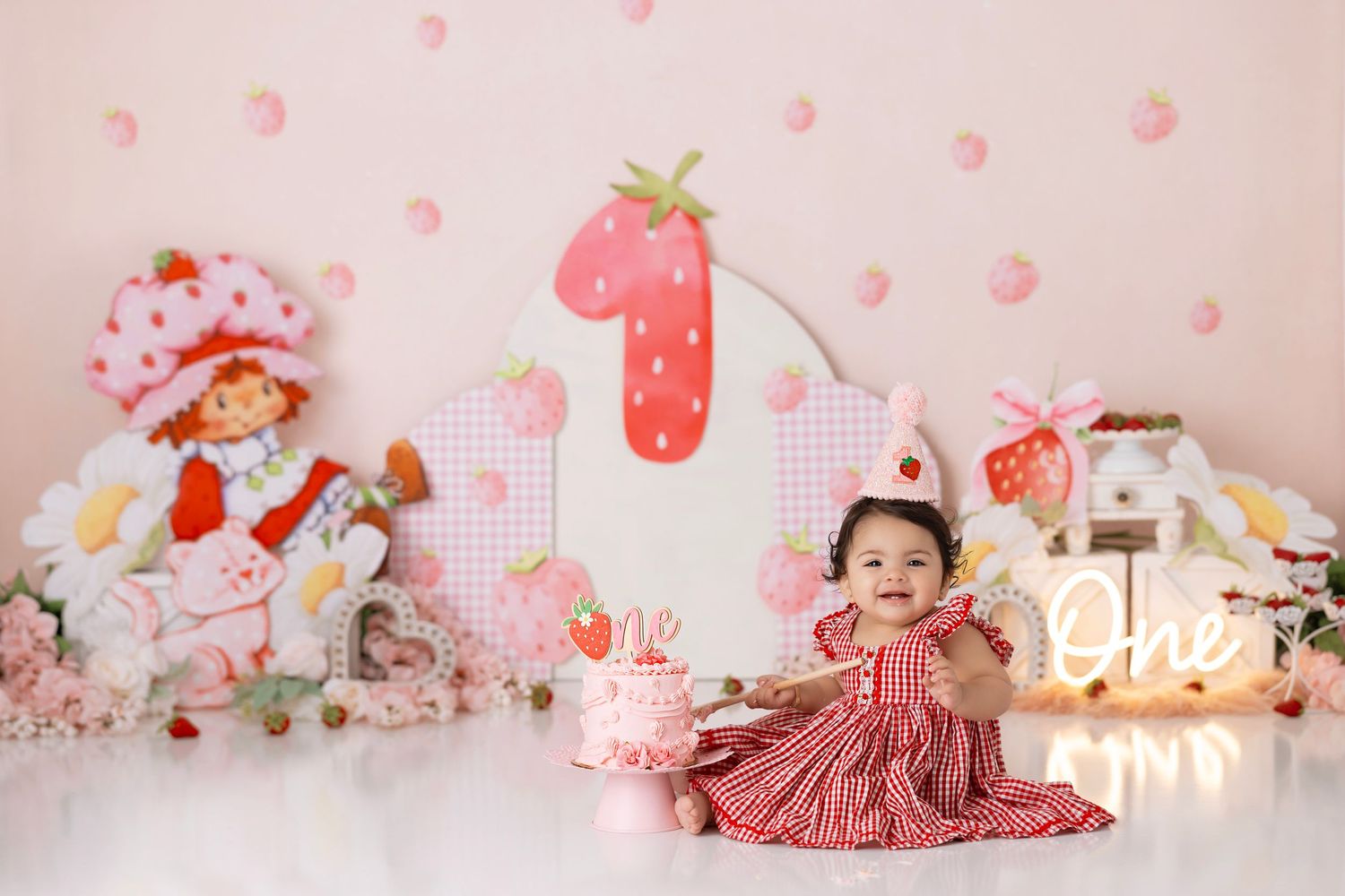 Sweet strawberry themed first birthday party setup with pink decor, plush toys and gingham dress.