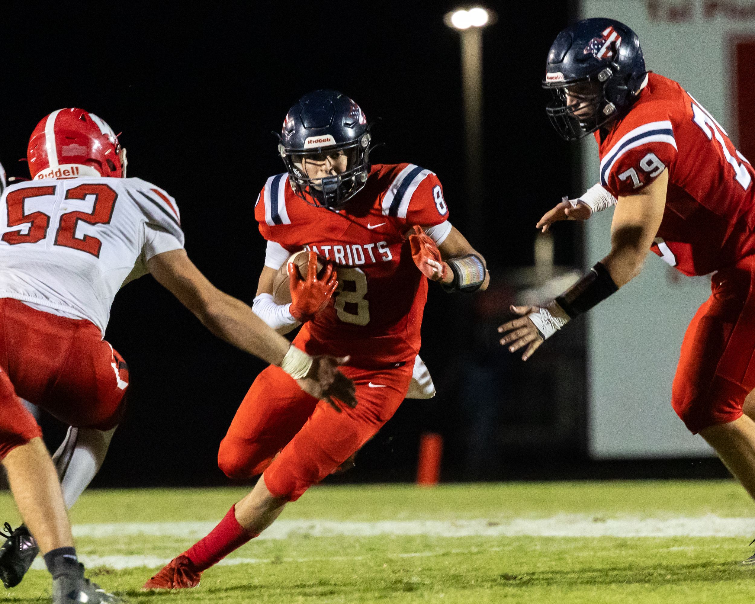 Patriots quarterback number 8 runs with ball during night football game.