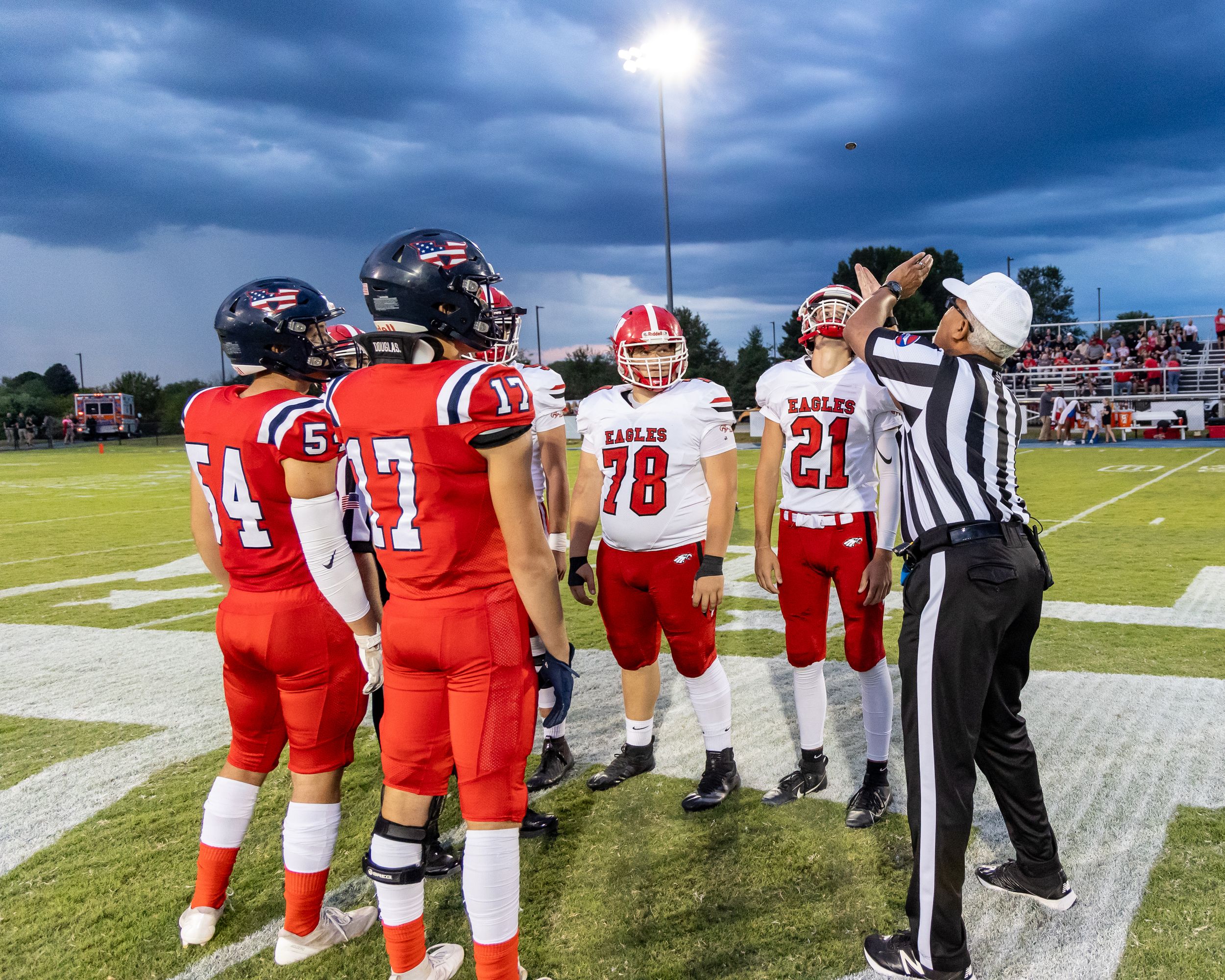 Football teams meet at midfield for coin toss with referee before stormy sky game.