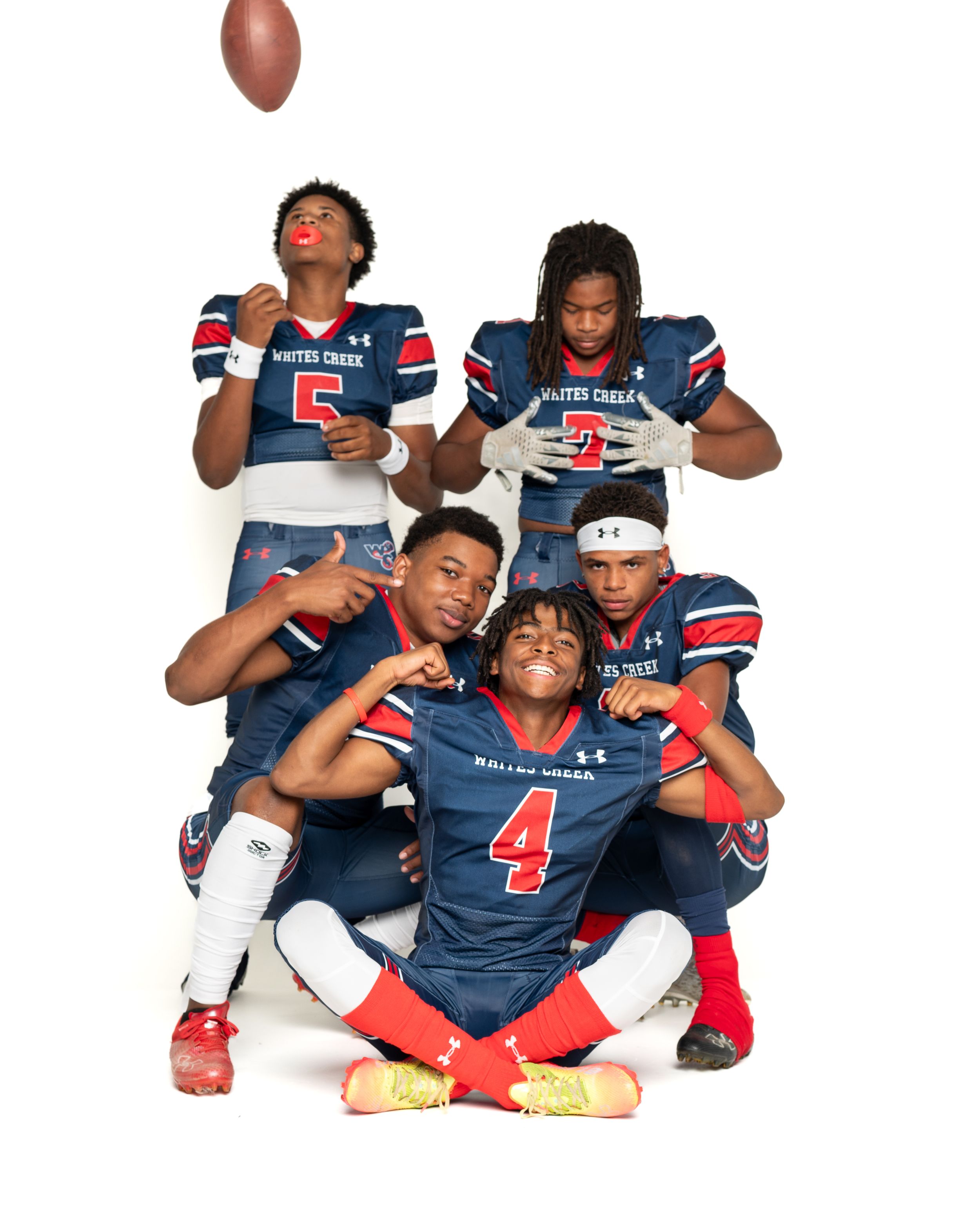 Four football players in blue Patriots uniforms pose together for team photo.