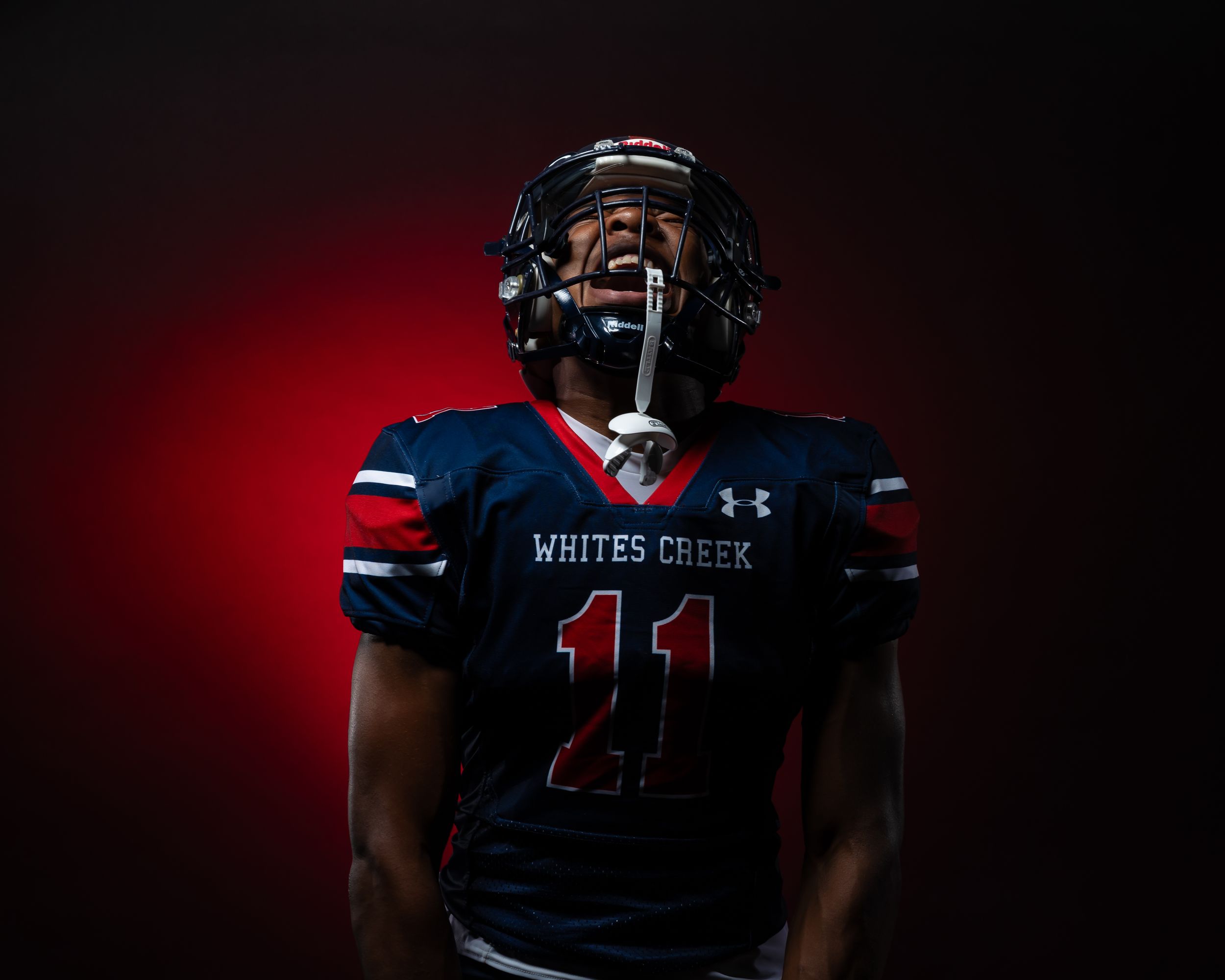 Whites Creek #11 football player in navy uniform poses dramatically in helmet against red background.