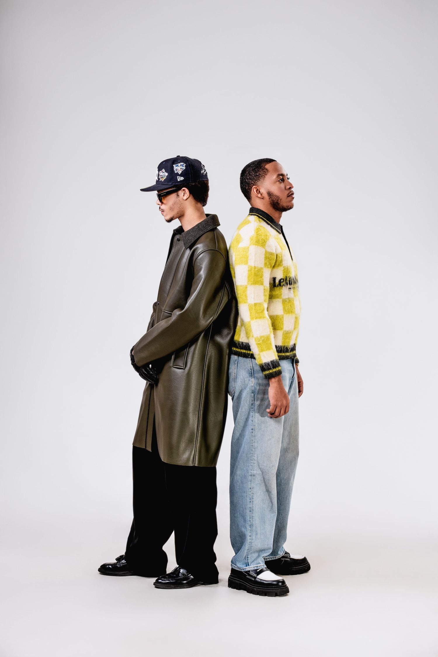 Fashion-forward editorial portrait of two models in stylish outfits, posing against a minimalist white backdrop.