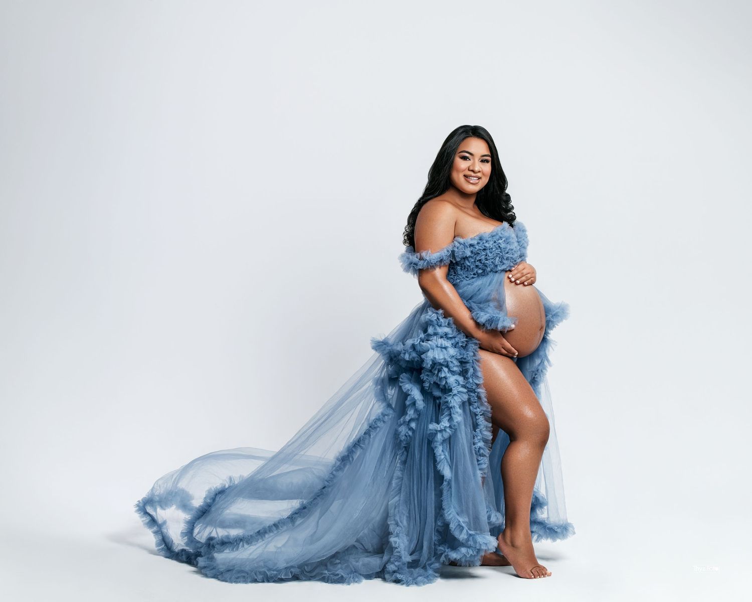 Maternity portrait featuring a mother in a flowing blue gown, embracing the beauty of motherhood in a minimalist studio setting.