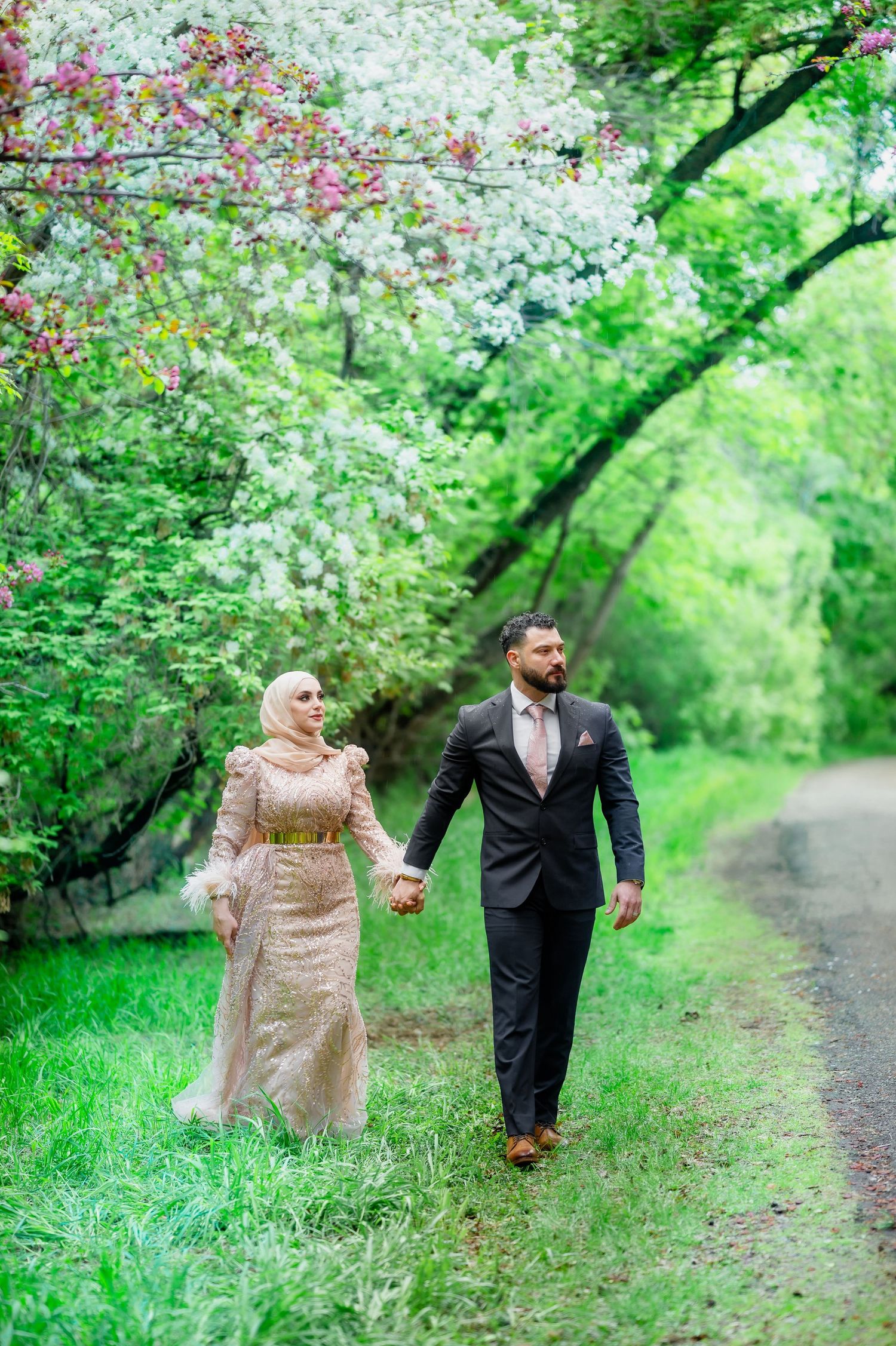 A couple walking hand in hand along a path under blooming spring trees.
