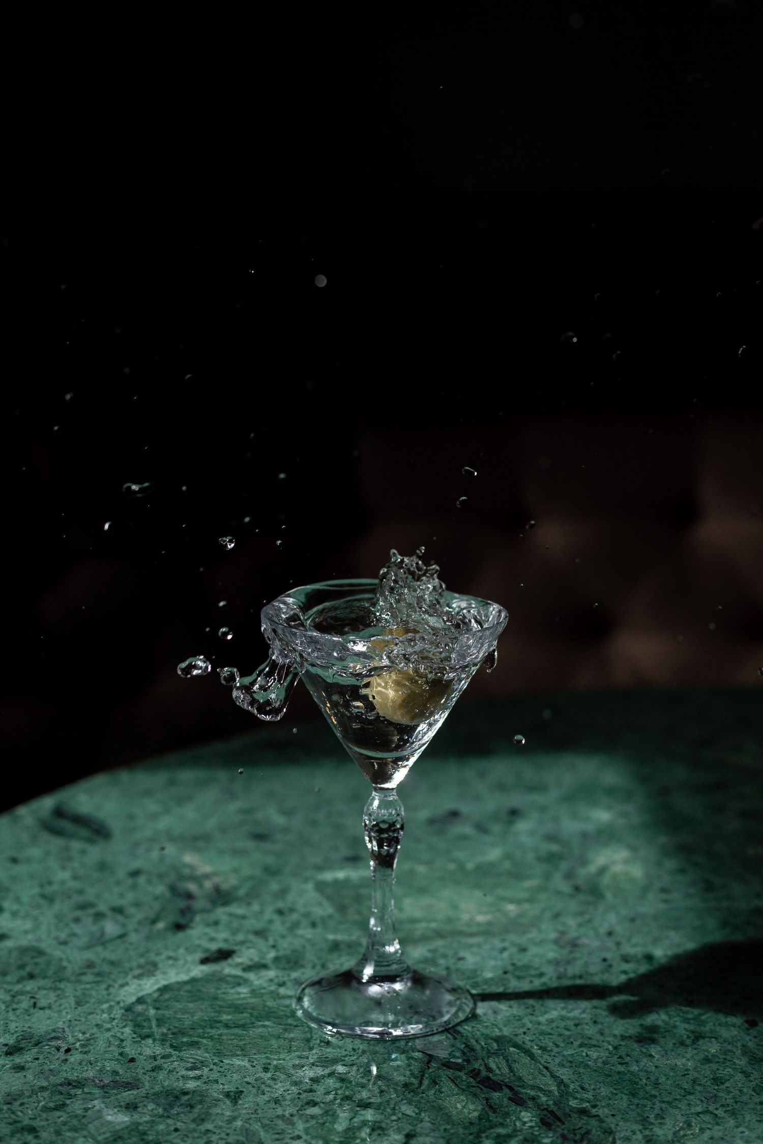 High-speed photograph of liquid splashing from a martini glass on green surface.