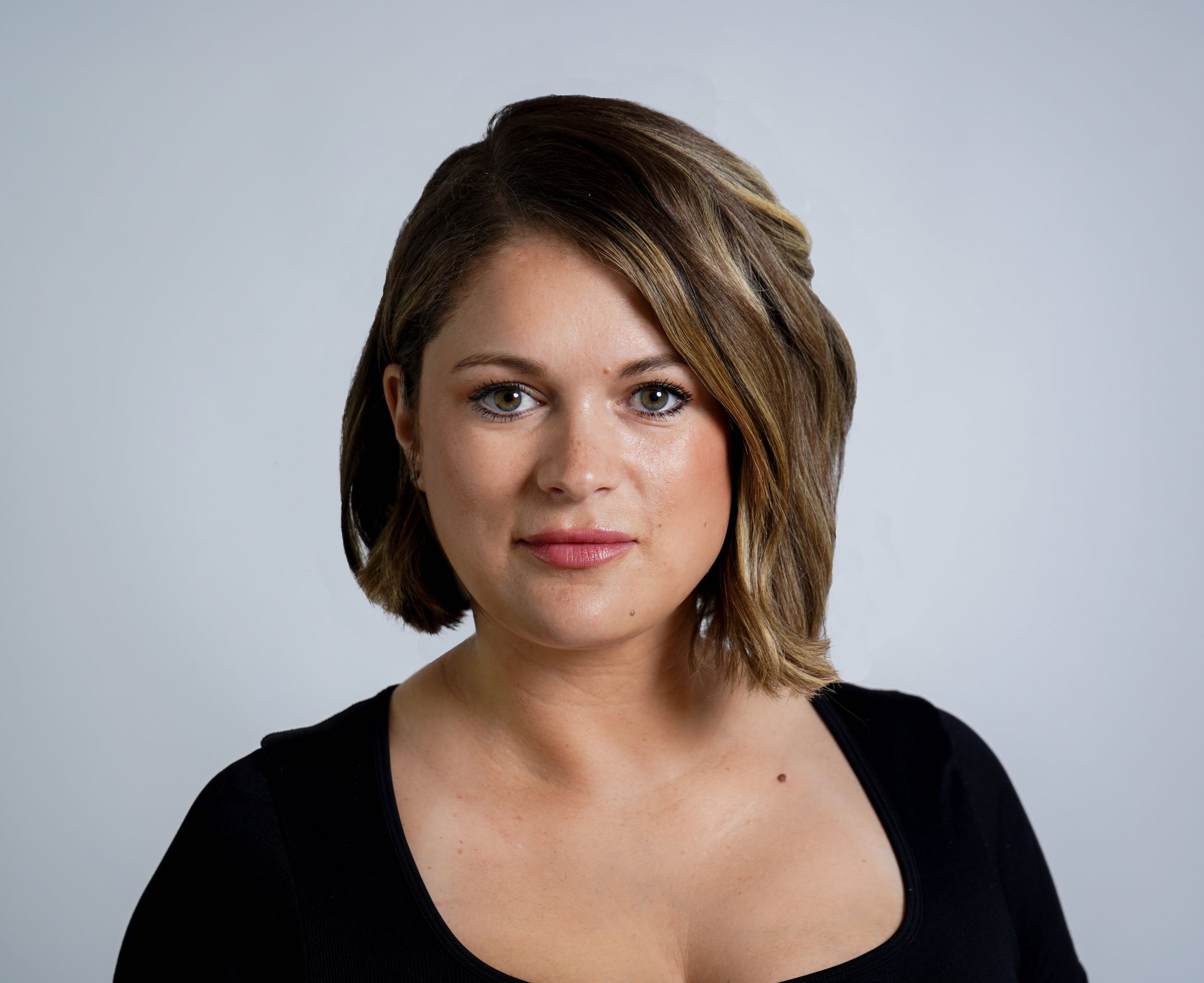 Professional headshot with short brown hair wearing a black top against a light gray background.