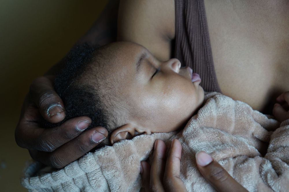 A peaceful newborn baby sleeping while breastfeeding, cradled in mother's arms wrapped in a soft blanket.