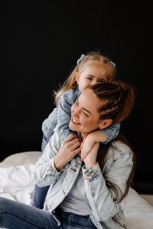 A tender moment captured between a parent and child wearing denim jackets against a dark backdrop.