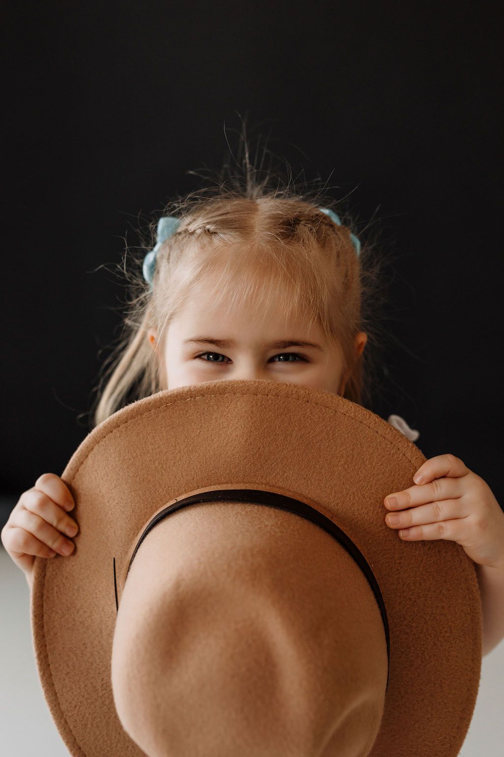 A playful portrait of someone peeking over a brown felt hat against a dark backdrop.