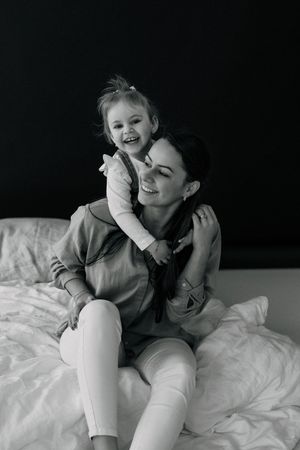 An intimate black and white portrait capturing a joyful embrace on white bedding.