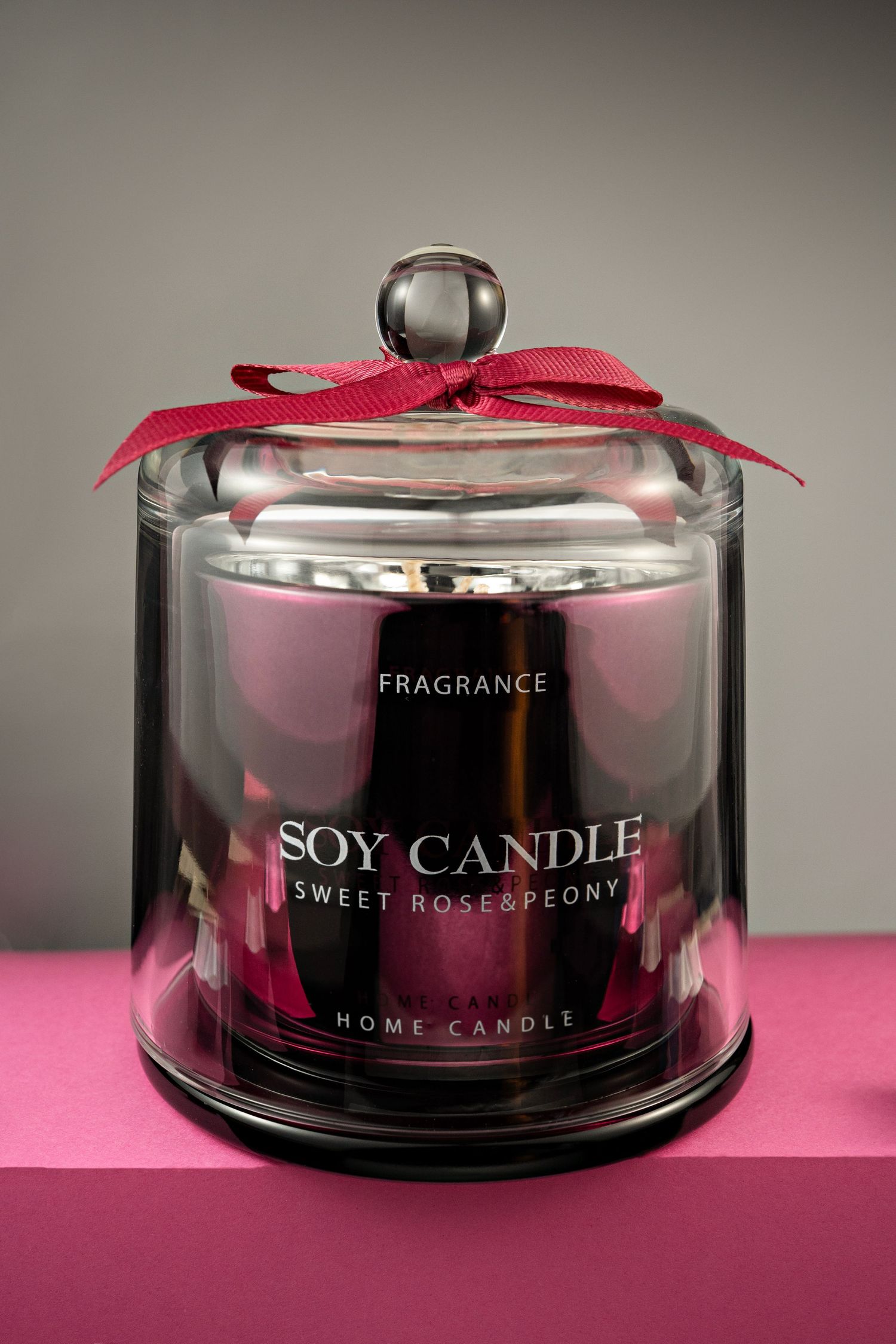 A pink soy candle in glass jar with red ribbon displays 'Sweet Rose Peony' fragrance under glass cloche dome.
