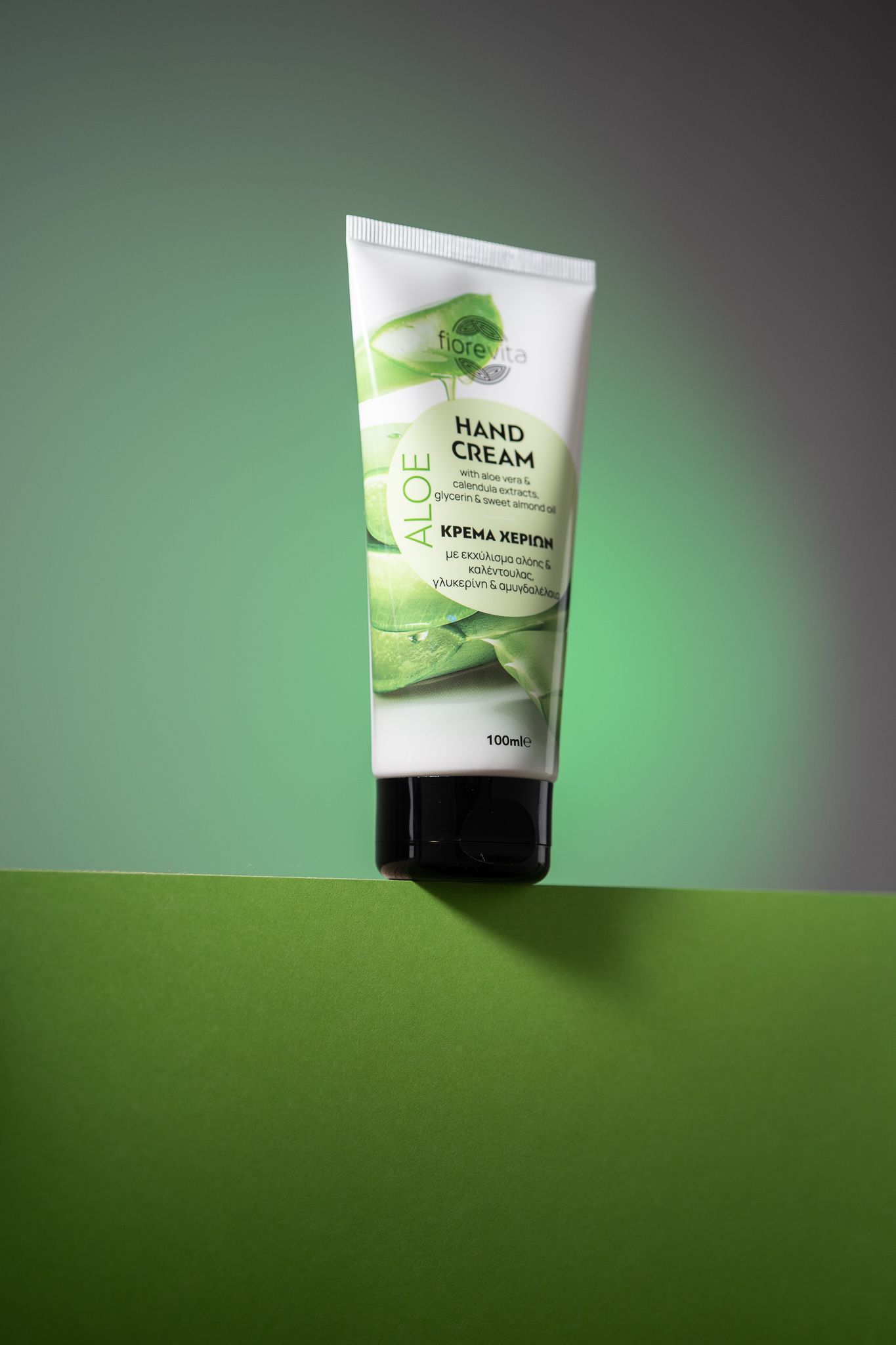 Hand cream product tube photographed against green background with dramatic lighting and shadow effects.