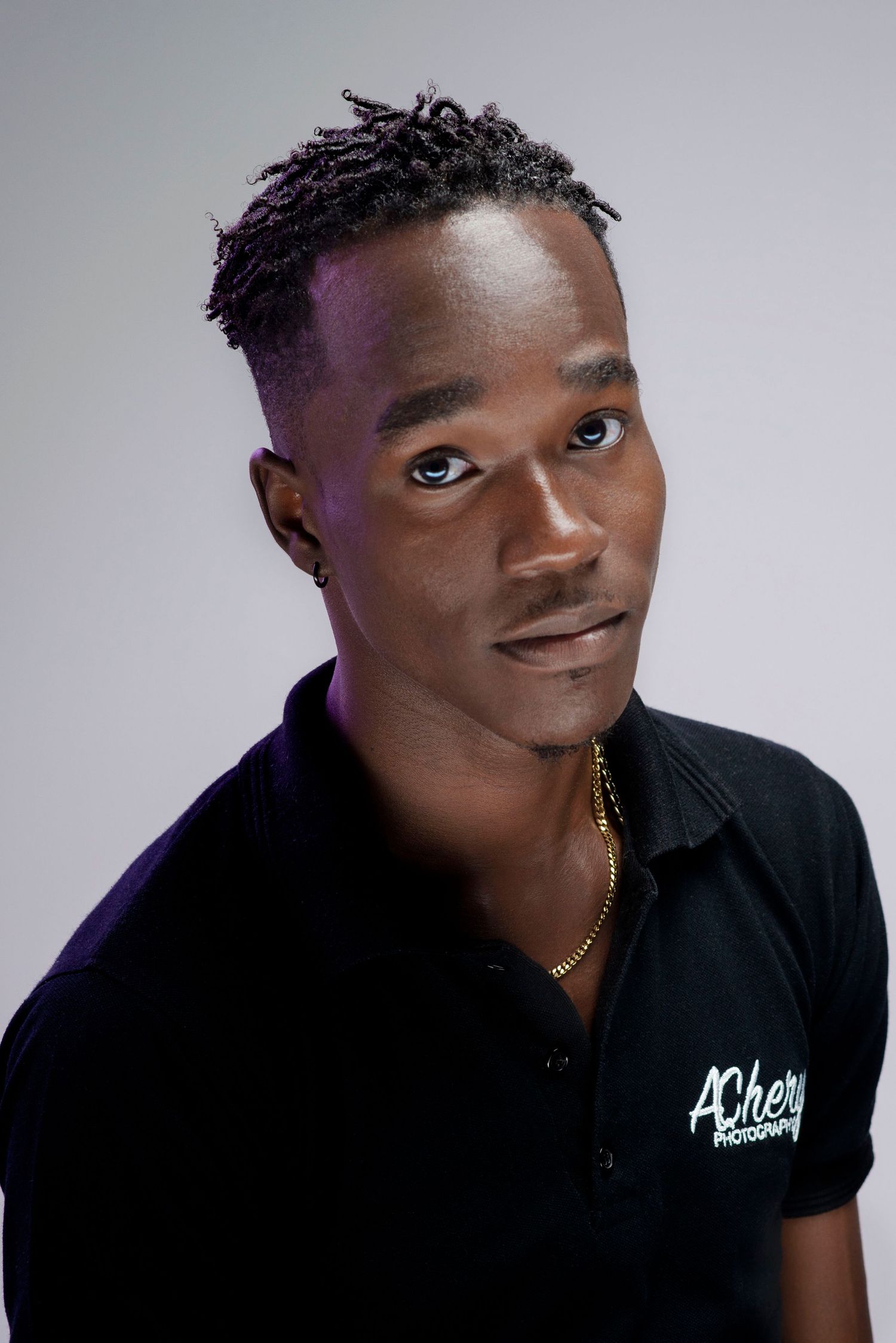 Portrait of a person in a white polo shirt with logo against a golden sparkly backdrop.