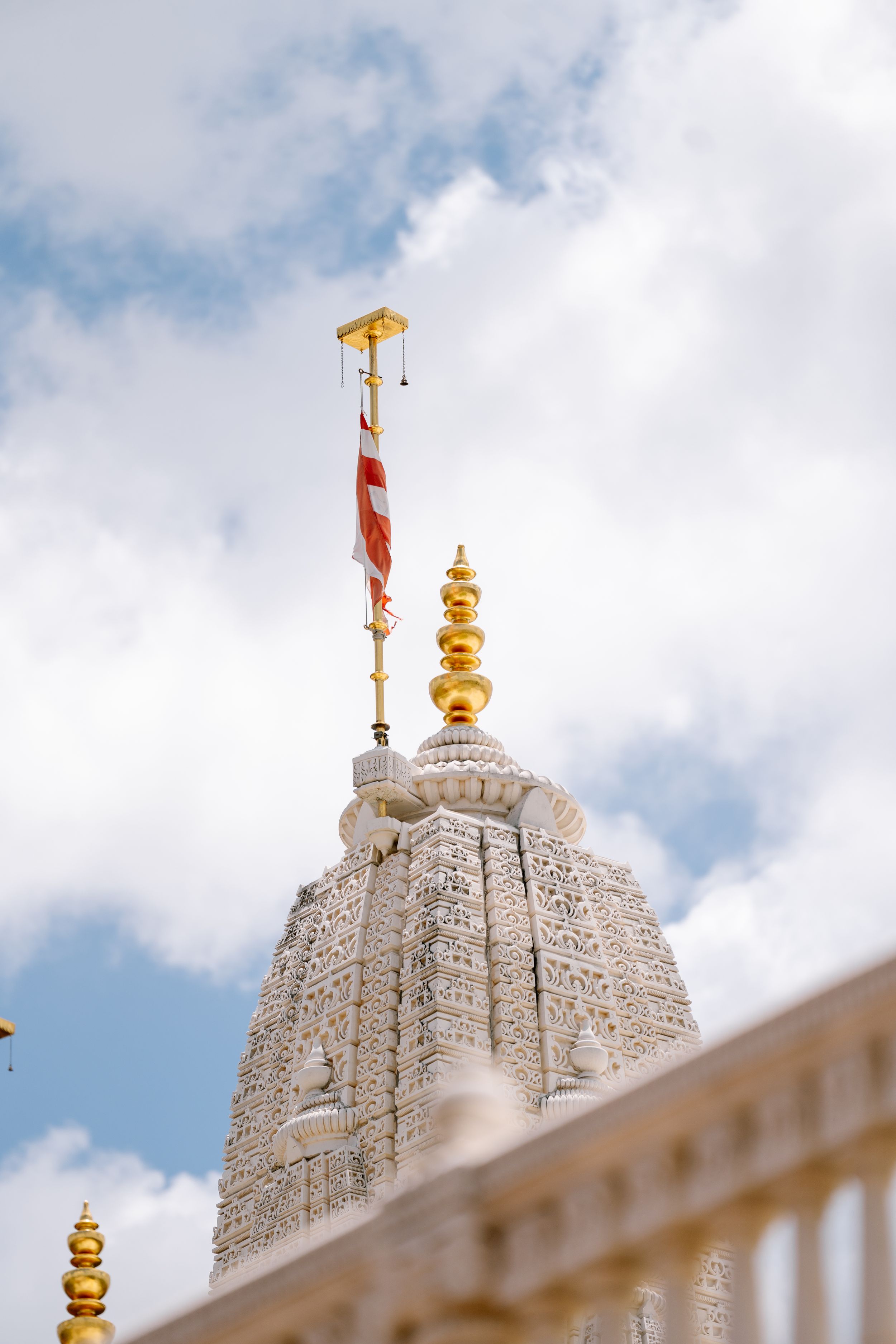 Ornate white temple spires with golden finials rise against a cloudy blue sky at BAPS Shri Swaminarayan Mandir, Atlanta.