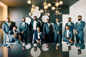 Wedding party in blue suits posing together in a stylishly lit indoor venue.