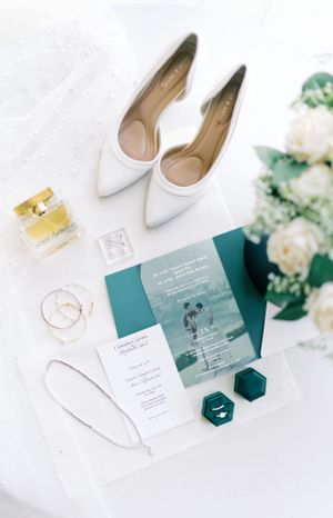 Wedding details flatlay with white shoes, teal invitations, and floral accents.