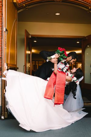 A dip pose featuring flowing white wedding dress and red accessories at an indoor venue.