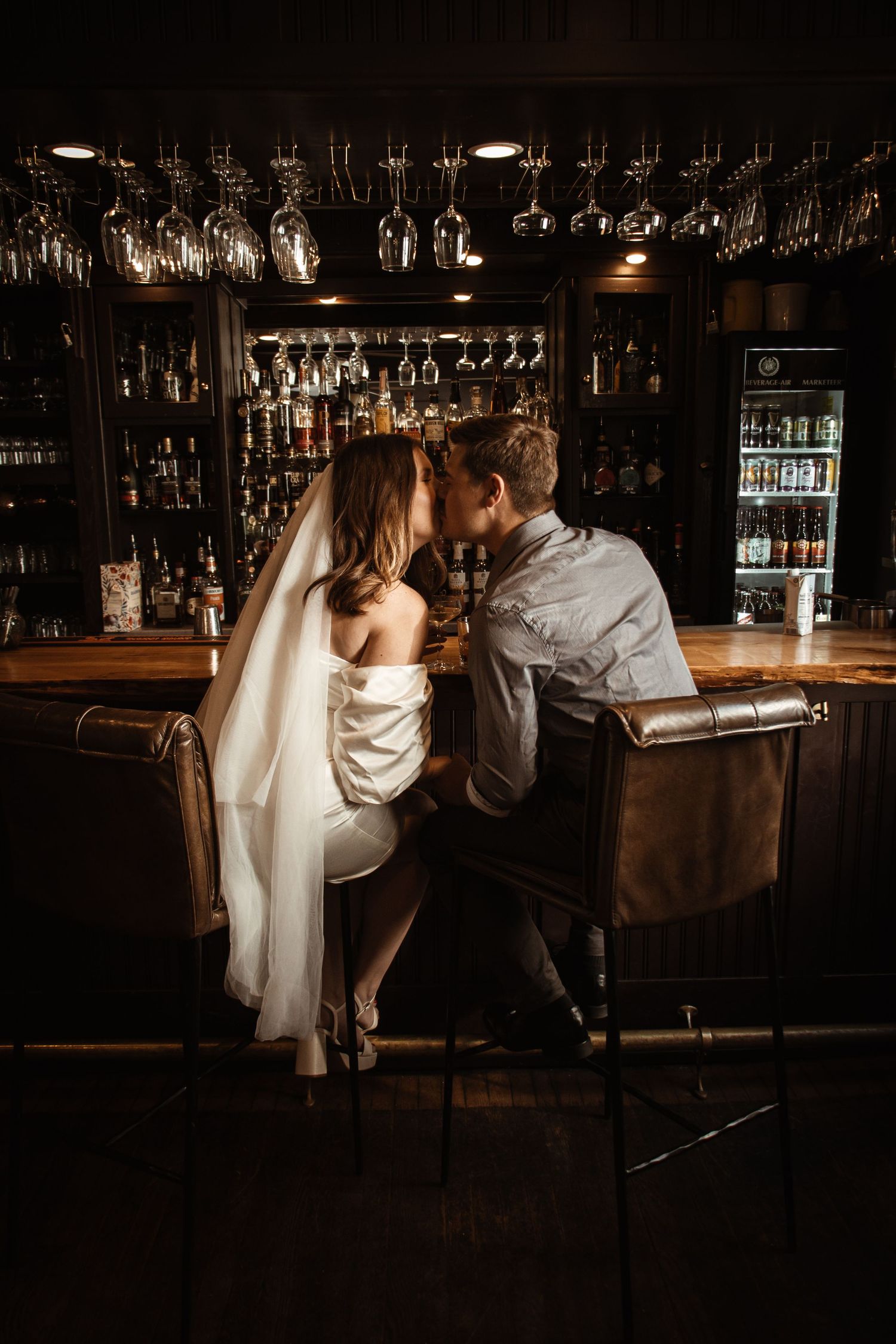 Romantic scene at a dimly lit bar with hanging glasses and bottles.