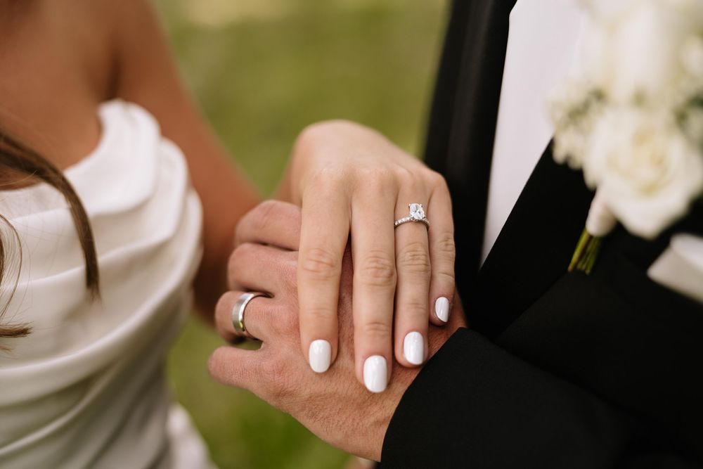 Close-up of bride and groom holding hands, showcasing diamond engagement ring and wedding bands on their wedding day.
