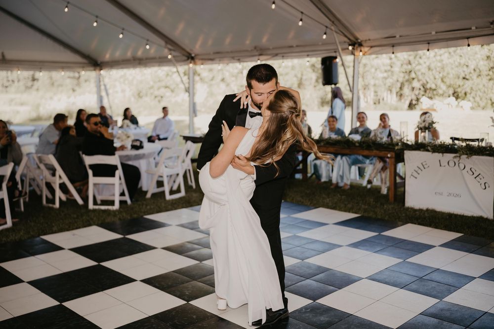 Bride and groom share their first dance on a black and white checkered floor under a white wedding tent.
