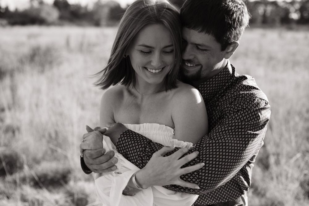 A couple embraces lovingly in a sunny field during an outdoor engagement photo session.