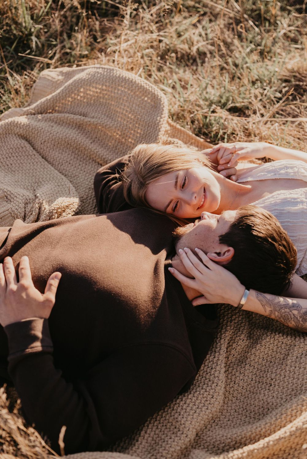 A couple lying on a knit blanket in golden sunlight creating an intimate outdoor moment.