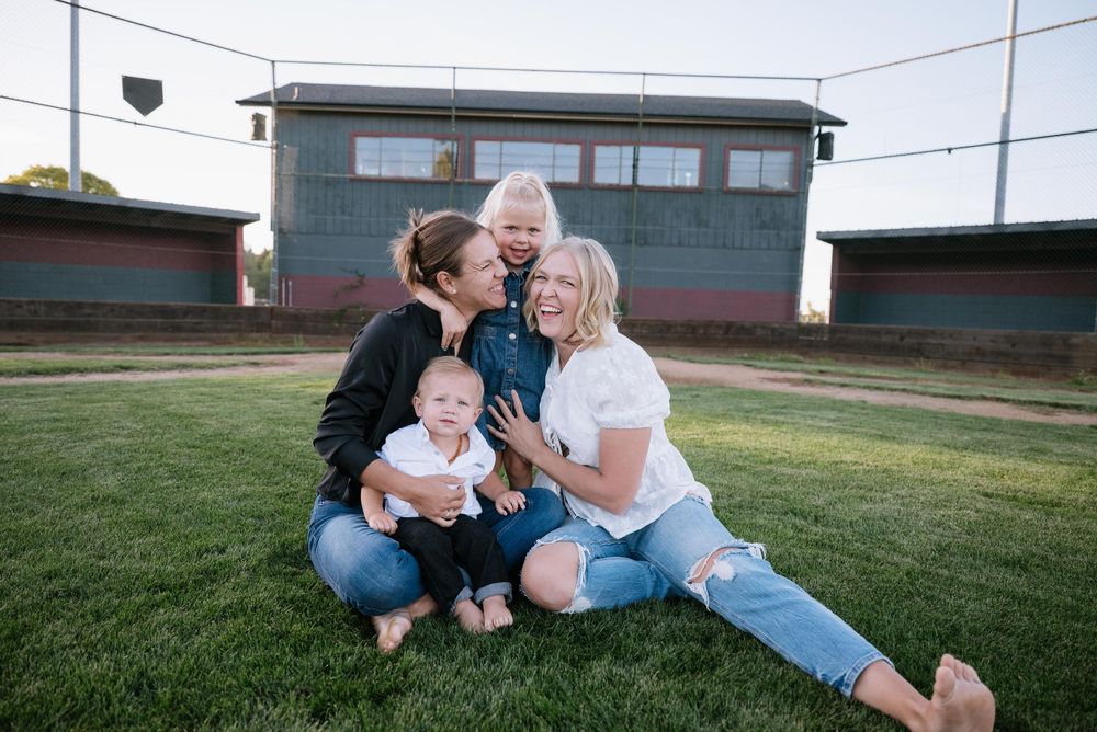 Family sits together on grassy lawn outside on sunny day enjoying quality time together.