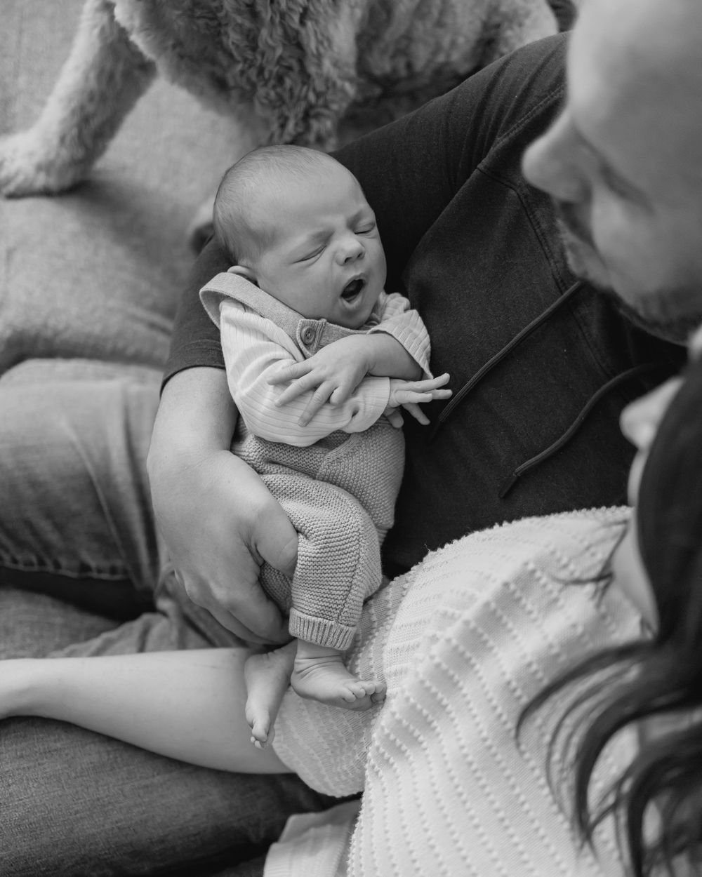 Black and white photo of a sleepy newborn baby yawning while cradled in fathers arms
