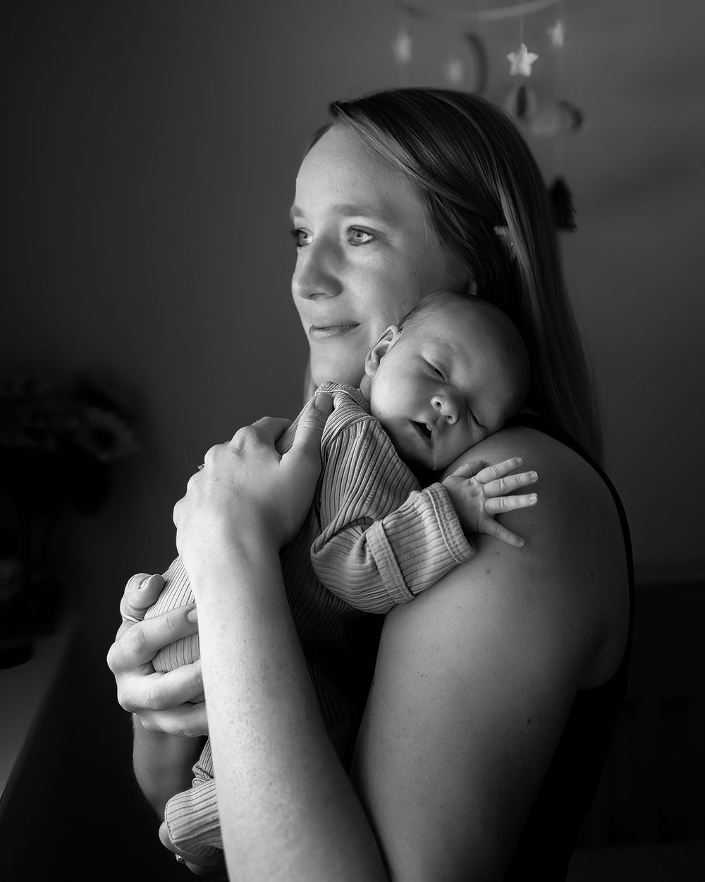 Black and white portrait of a mother holding her sleeping newborn baby in a tender embrace against her shoulder.