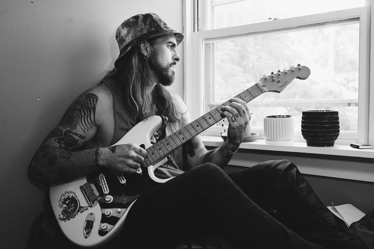Musicians with guitars pose near windows in moody black and white portraits.