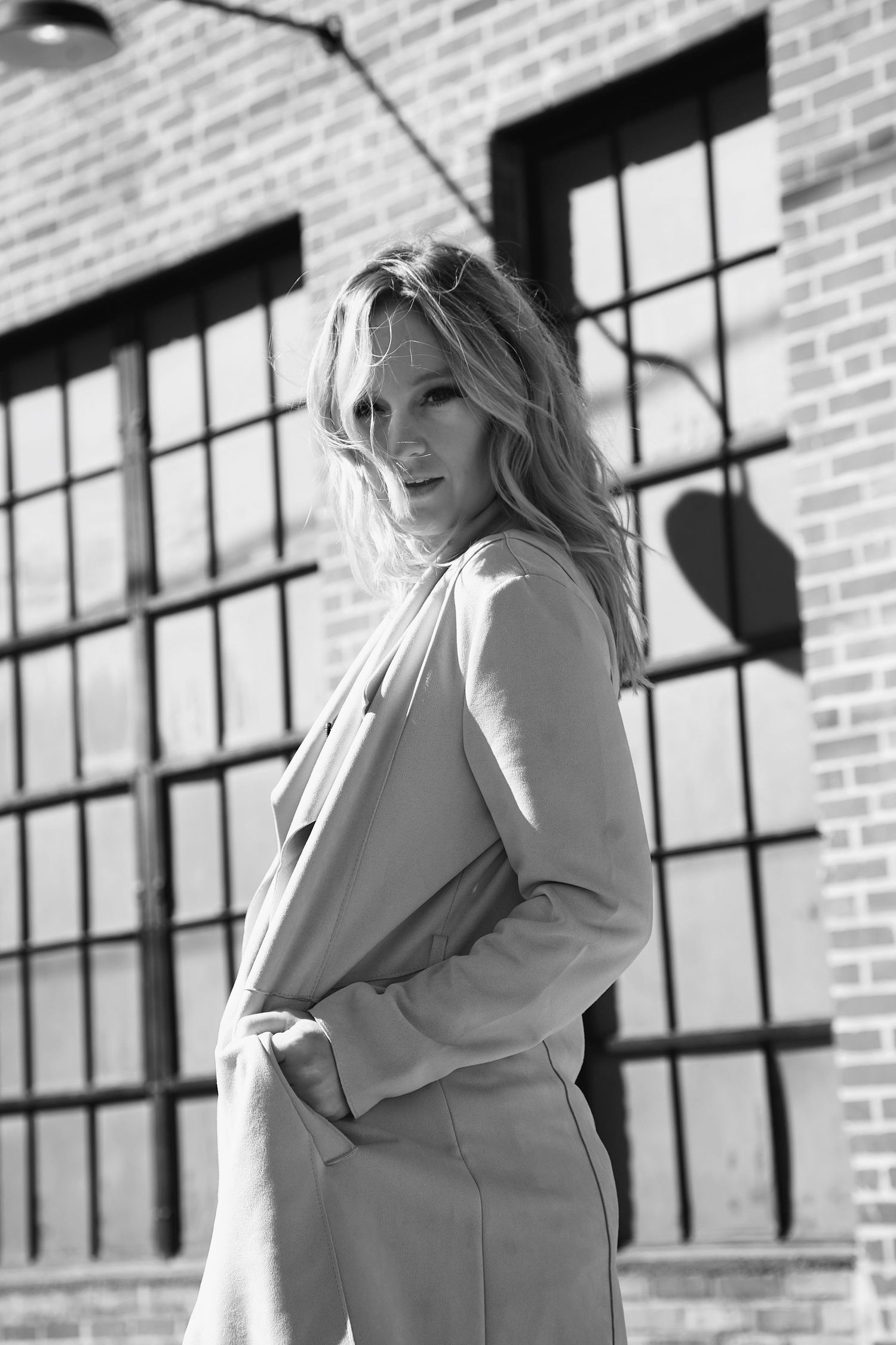Black and white portrait against industrial brick wall with windows.