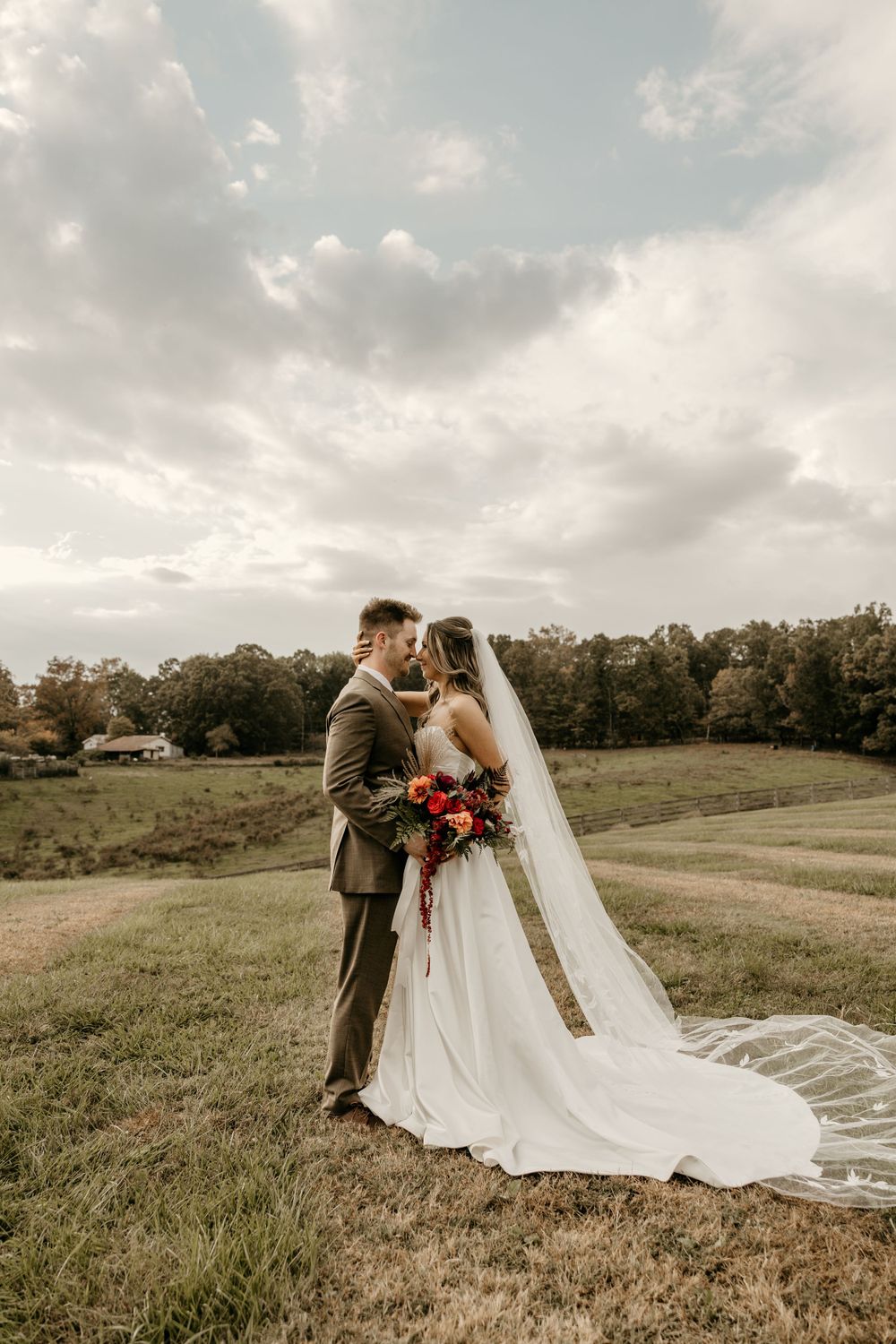 Wedding couple embracing in scenic field during golden hour with dramatic cloudy sky.