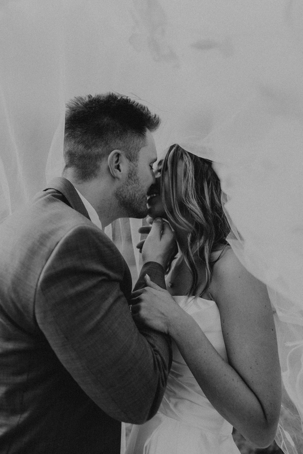 A romantic intimate moment captured between a couple beneath a white veil.