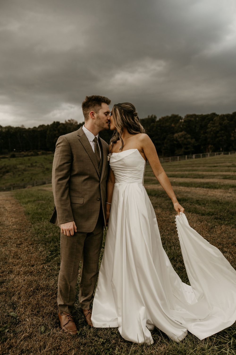 Dramatic wedding photo of couple on rural hillside with stormy sky and flowing white dress.