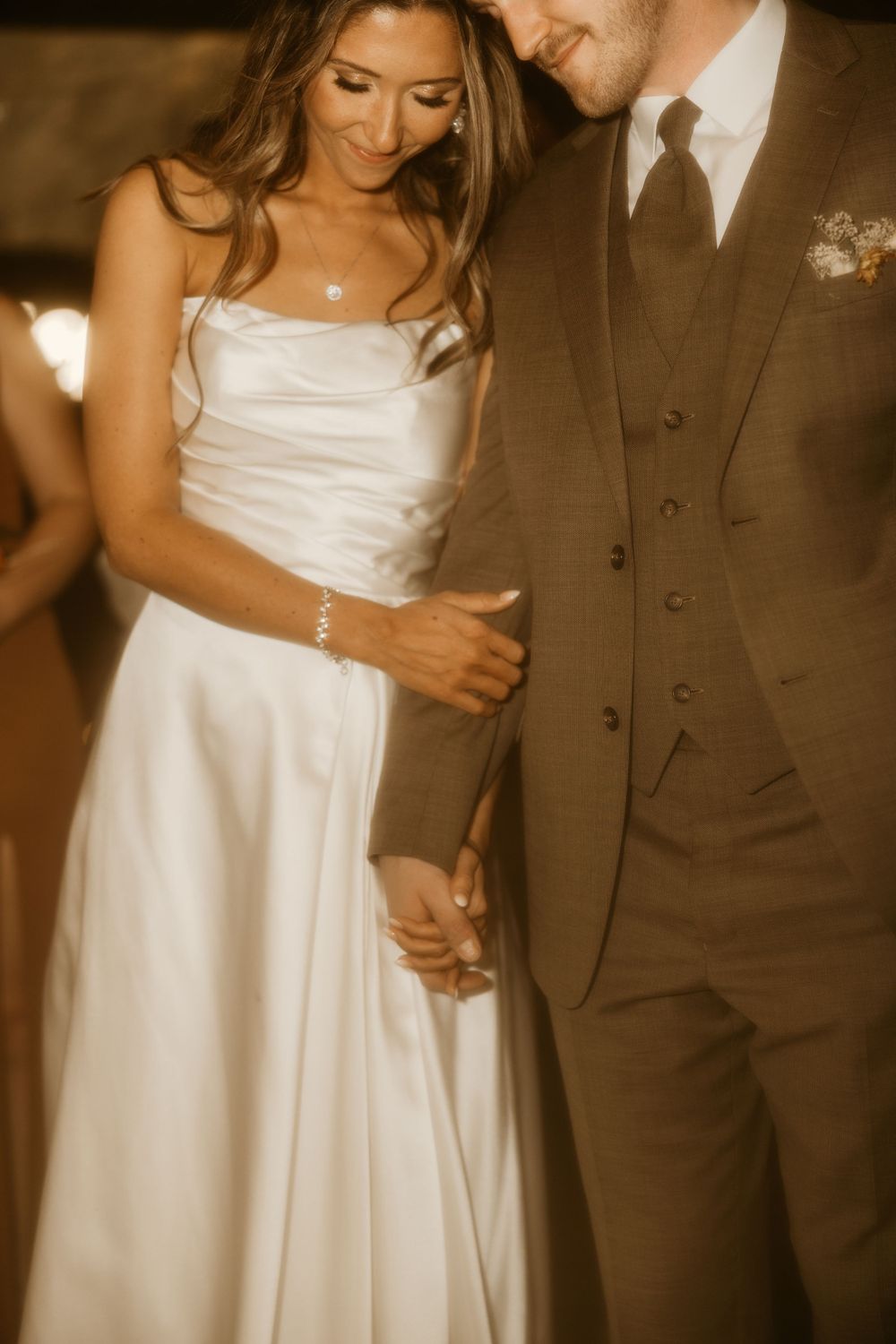 An intimate moment captured of a couple in wedding attire with warm sepia tones and romantic lighting.