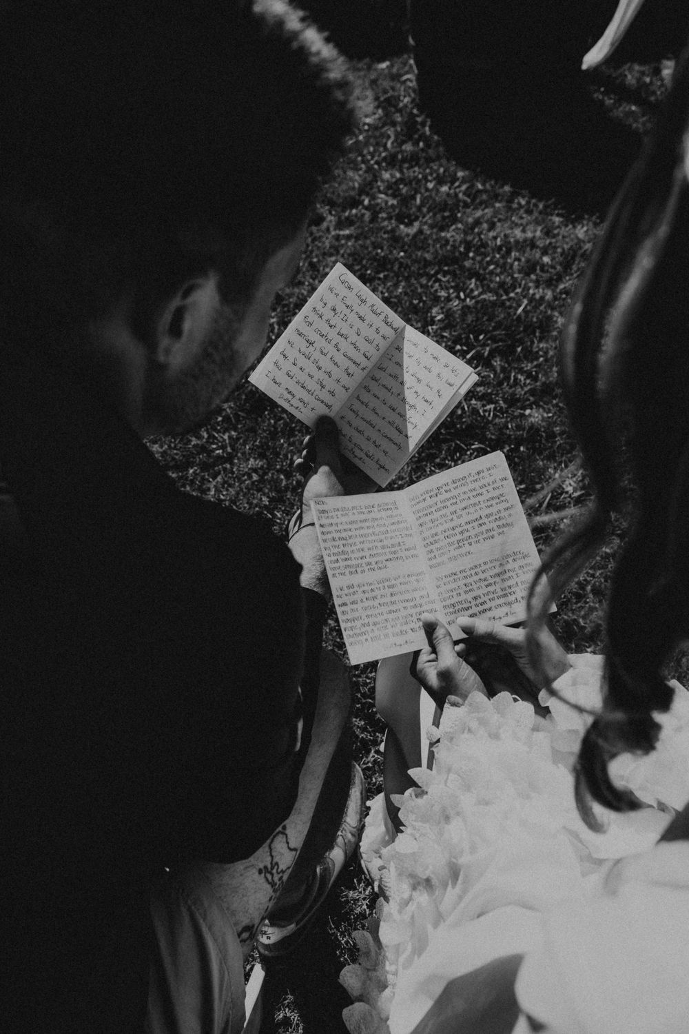 Overhead view of handwritten wedding vows or letters being written on paper outdoors in black and white.