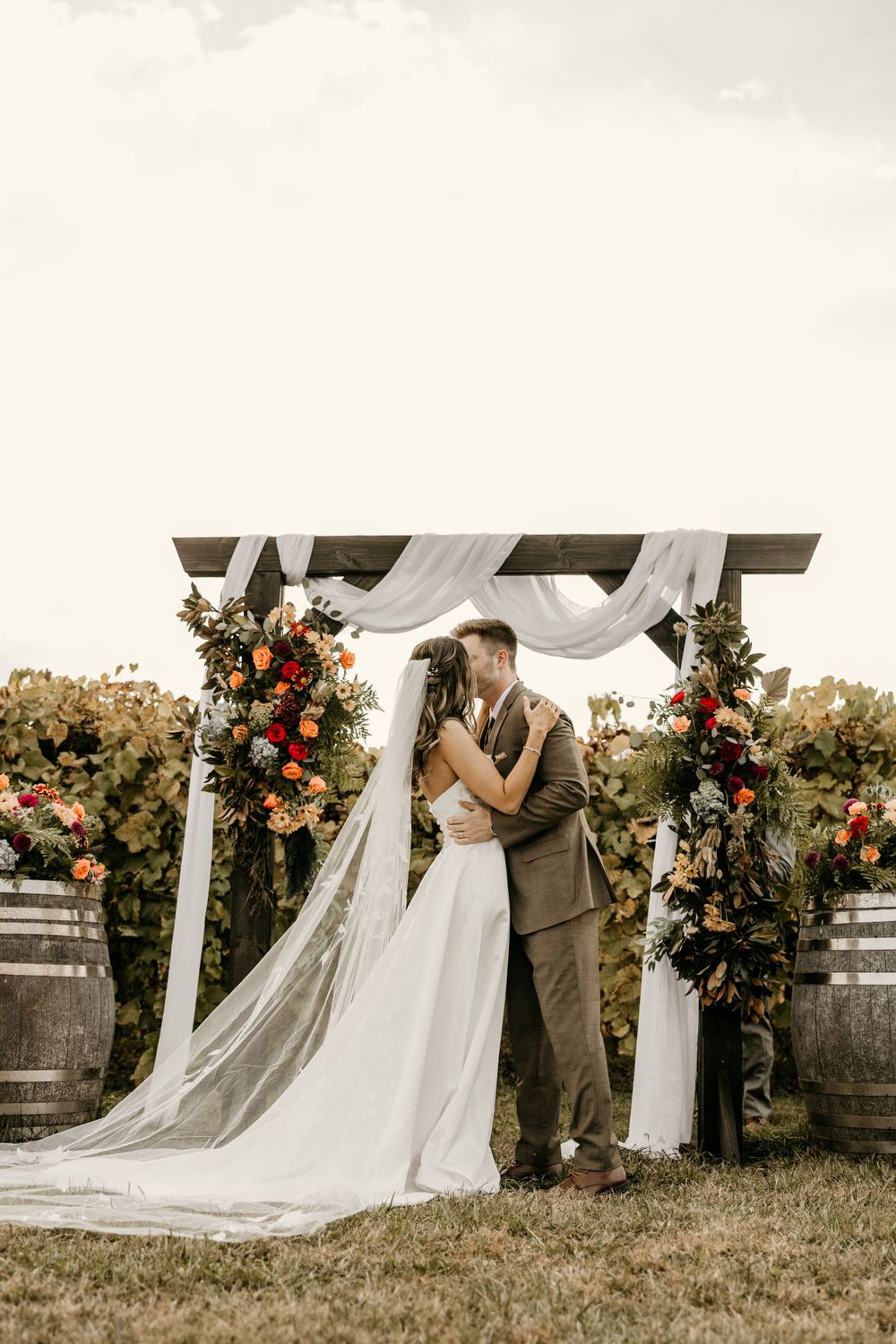 Romantic outdoor wedding ceremony under white draped arch decorated with colorful floral arrangements.